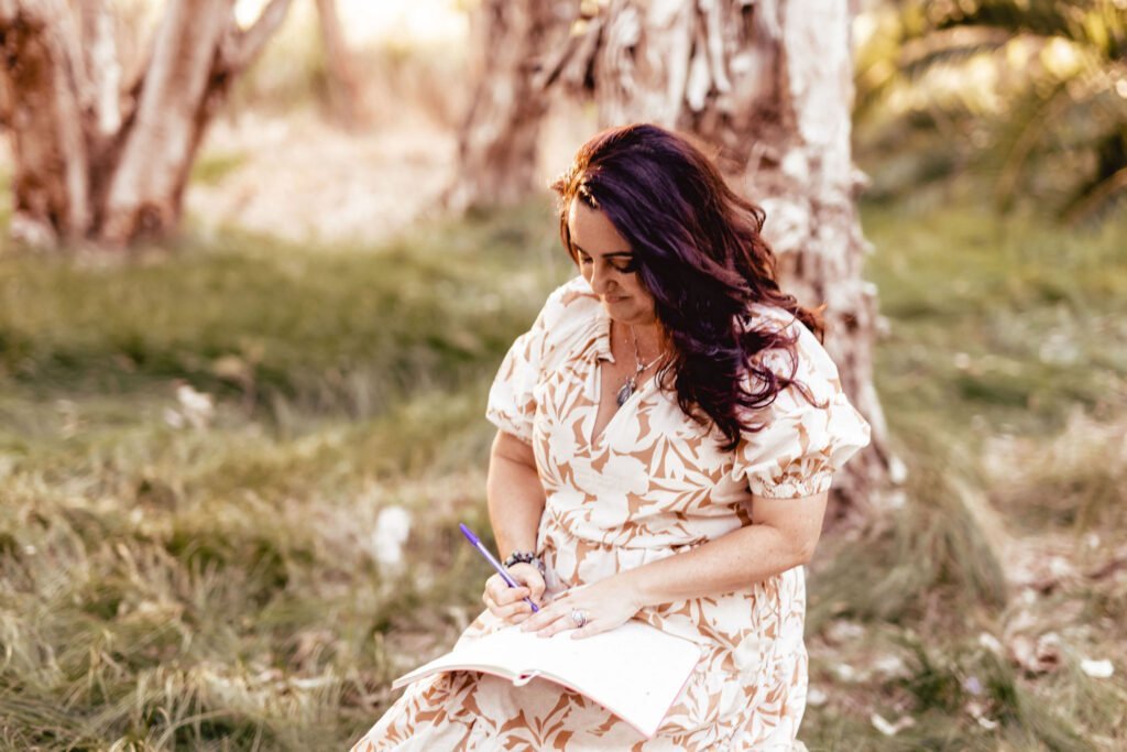 Tess sitting outside in a forest journaling